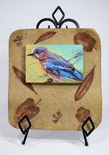 Load image into Gallery viewer, Backyard Bluebird painting by Pat Cross mounted in a handbuilt and kiln fired stoneware frame resting on a black metal easel.