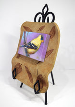 Load image into Gallery viewer, Alluring Goldfinch original painting by Pat Cross mounted in a handbuilt kiln fired stoneware frame and resting on a black metal easel facing left.
