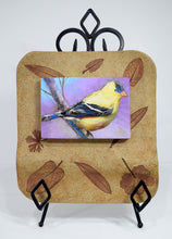 Load image into Gallery viewer, Alluring Goldfinch original painting by Pat Cross mounted in a handbuilt kiln fired stoneware frame and resting on a black metal easel.
