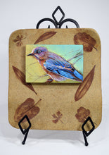 Load image into Gallery viewer, Backyard Bluebird painting by Pat Cross mounted in a handbuilt and kiln fired stoneware frame resting on a black metal easel.
