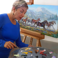 Load image into Gallery viewer, Pat Cross mixing paint to add the finishing touch to On the Move oil painting.
